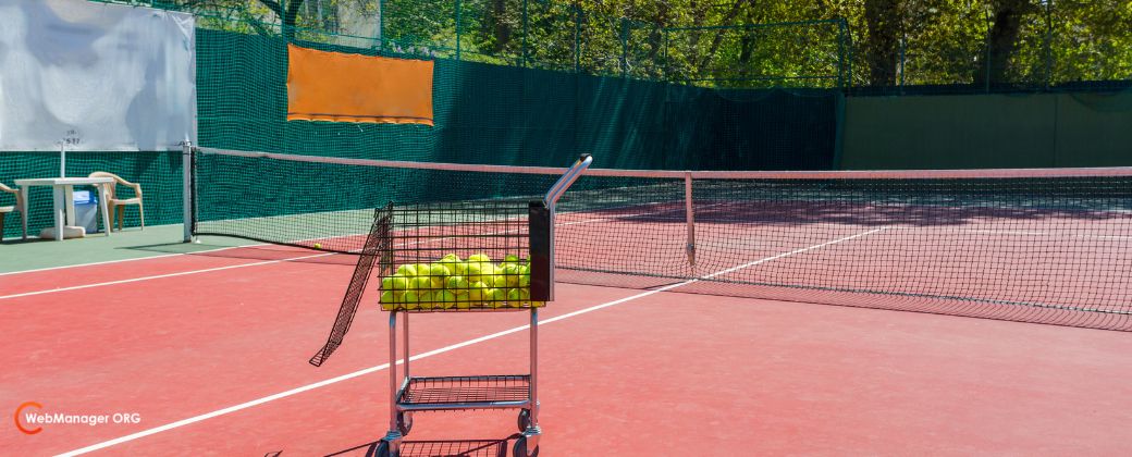 קירוי מגרשי ספורט - מגרש טניס עם עגלת כדורי טניס ובצד שמאל למטה לוגו אתר blog.webmanager.