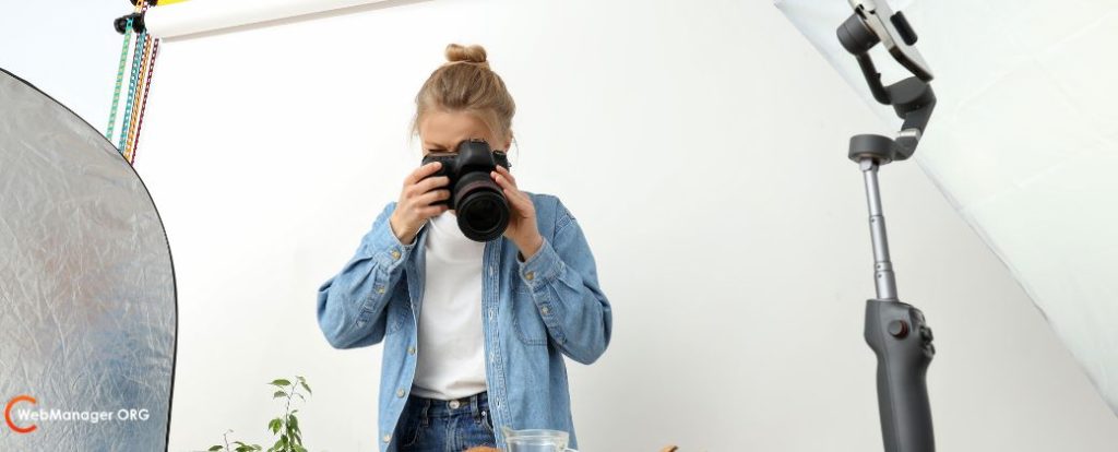 צילום למתחילים - ניתן לראות אישה בלונדינית אסופת שיער מכוונת את המצלמה מטה ובצד שמאל למטה לוגו אתר blog.webmanager